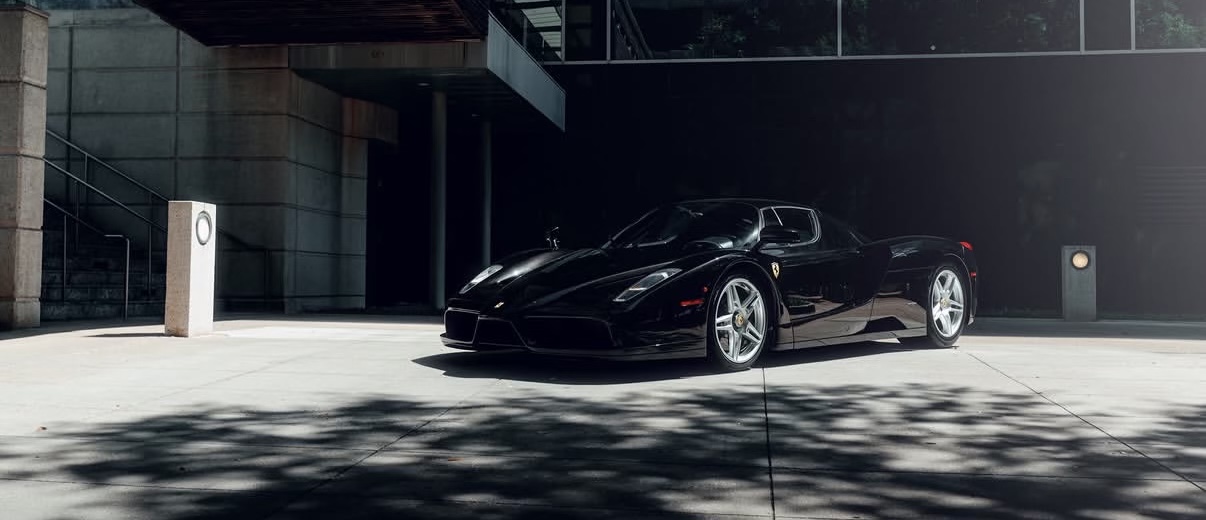 Black Ferrari Enzo, three-quarter front view, modern glass building behind